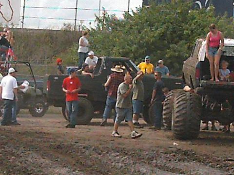 1986 Ford Bronco - A group of people watch as trucks and an ATV are in a muddy area, possibly at an event.