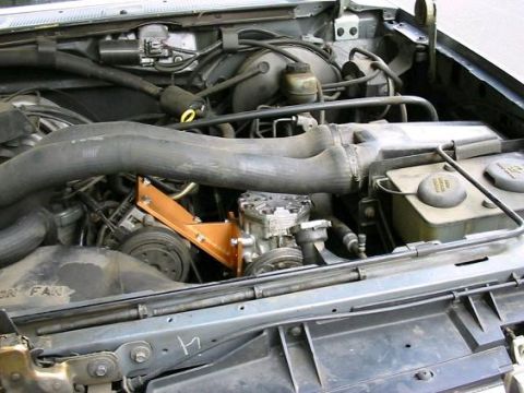 1993 Ford Bronco - Engine bay shot of a York-style onboard air compressor mounted low on the passenger side with a fabricated orange-painted bracket and a dri…
