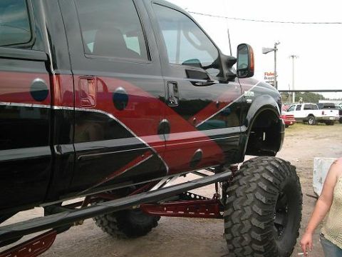 1986 Ford Bronco - A heavily modified pickup truck with custom graphics is parked outdoors, with other vehicles visible in the background.