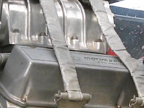 1986 Ford Bronco - Close-up of an engine part with V8 power branding and metallic straps.