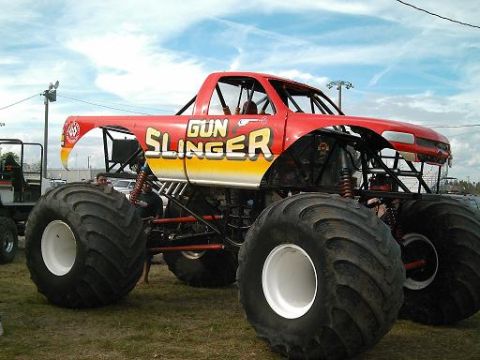 1986 Ford Bronco - Monster truck named "Gun Slinger" with custom paint and massive tires sits on display.
