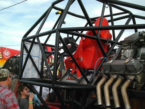 1986 Ford Bronco - A custom-built vehicle with a prominent roll cage, red racing seat, and a powerful engine is displayed outdoors.