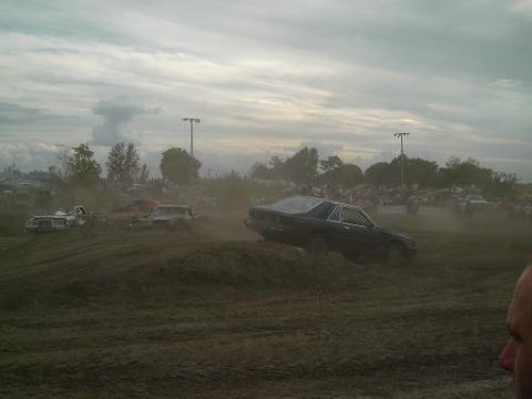 1986 Ford Bronco - Cars are seen in a dusty field during an event with spectators in the background.