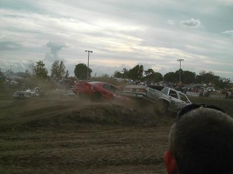 1986 Ford Bronco - Cars compete in a demolition derby event, kicking up dust on the track.