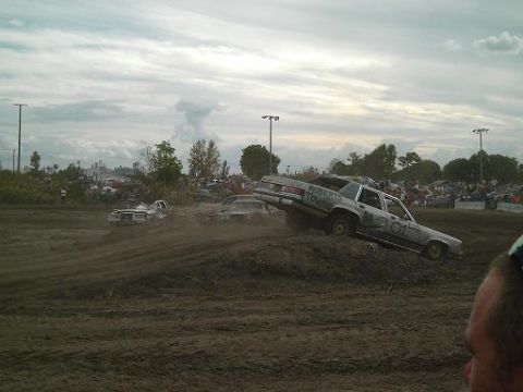 1986 Ford Bronco - Cars compete in a demolition derby event with spectators in the background.
