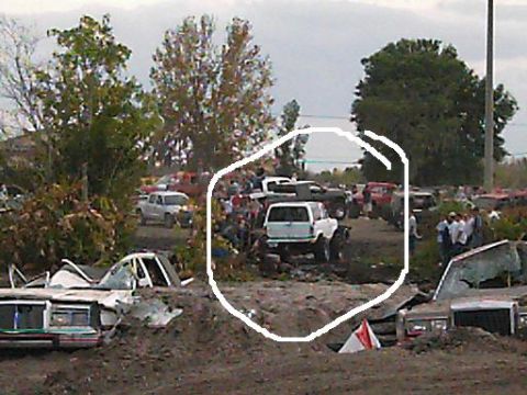 1986 Ford Bronco - A crowd gathers around a white pickup truck in a muddy outdoor event.