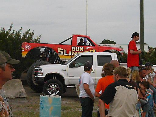 Red monster truck "GUN SLINGER" over white pickup truck