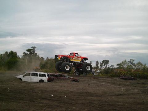 1986 Ford Bronco - Monster truck "Gun Slinger" airborne over wrecked vehicles during an event.