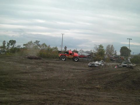 1986 Ford Bronco - A monster truck event with multiple vehicles in a dirt arena under a cloudy sky.