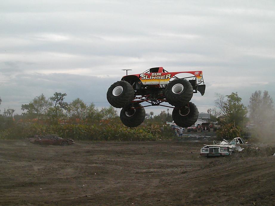Monster truck 'Gun Slinger' airborne over a dirt track with other vehicles in the background