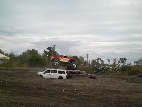 1986 Ford Bronco - A monster truck named "Gun Slinger" leaps over a white van and a red car in a demolition derby event.