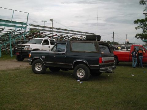 1986 Ford Bronco - Ford Bronco parked on grass with other trucks nearby under a cloudy sky.