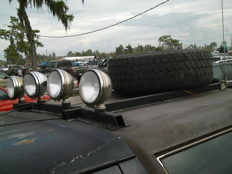 1986 Ford Bronco - A vehicle with a roof rack, spare tire, and auxiliary lights is parked outdoors among other vehicles.
