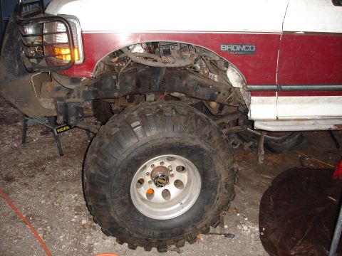 1989 Ford Bronco - A red and white Ford Bronco is shown with its front end partially dismantled, revealing the chassis and suspension components.