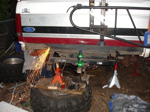 1989 Ford Bronco - A person is using a grinder to cut the rear bumper of a Ford truck, which is supported by jack stands.