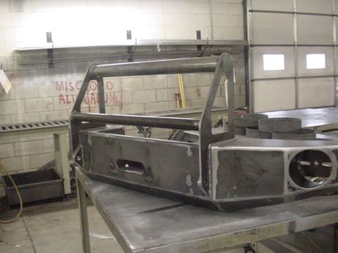1993 Ford Bronco - Unfinished custom steel winch bumper with brush guard is shown on a workbench in a workshop.