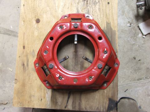 1965 Ford Mustang - A red clutch pressure plate is shown on a wooden board, with visible bolts and springs.