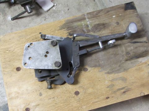 1965 Ford Mustang - A close-up view of a carburetor linkage assembly, likely for an older vehicle, is shown on a wooden surface.