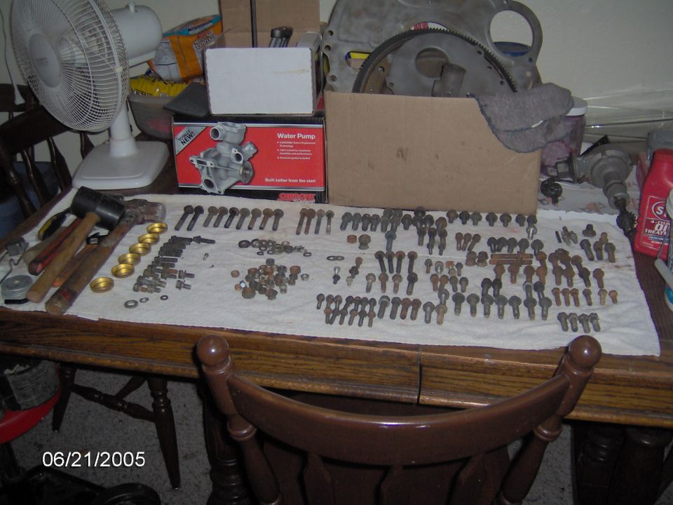 Table with assorted bolts, washers, and engine parts including a water pump box and a flywheel