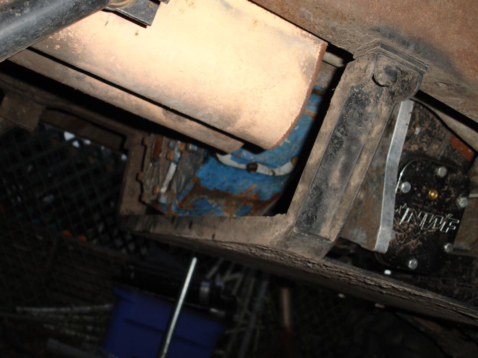 Underside view of vehicle showing exhaust pipe, blue-painted component, and a black metal bracket with a silver plate labeled 'INNF'