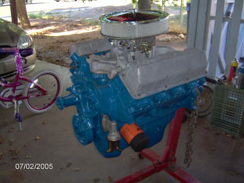 1978 Ford Bronco - A blue V8 engine is mounted on a red engine stand, with a bicycle and part of a car visible in the background.
