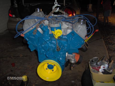 1978 Ford Bronco - A blue engine is being hoisted, with a car's trunk visible behind it.