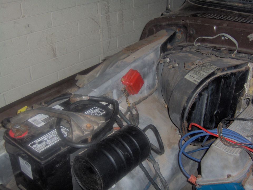 Car battery, air filter, and engine components in engine bay. Some wiring and a red distributor cap are visible