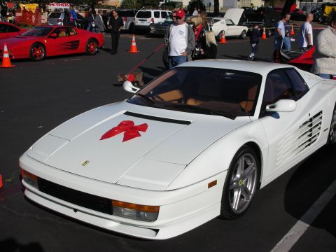 1992 Ford Crown Victoria - White Ferrari Testarossa with a red bow on its hood, parked at an outdoor event with other cars.