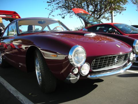 1992 Ford Crown Victoria - A classic maroon Ferrari 250 GT Berlinetta is parked next to another red vehicle under a clear blue sky.