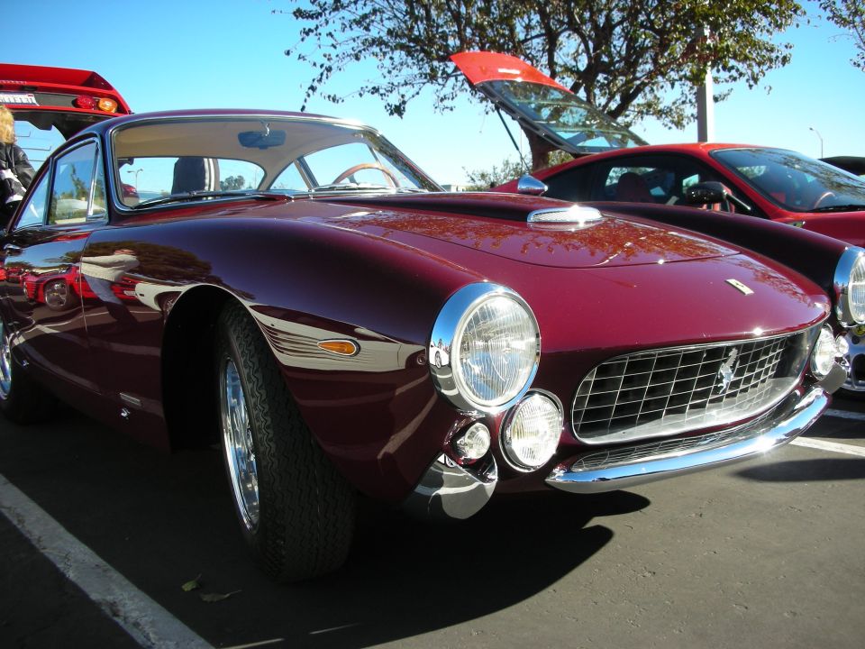 Maroon Ferrari 250 GT Berlinetta parked next to a red car with its trunk open