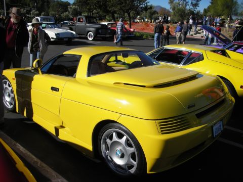 1992 Ford Crown Victoria - A bright yellow sports car is parked at an outdoor event, with other vehicles and people in the background.