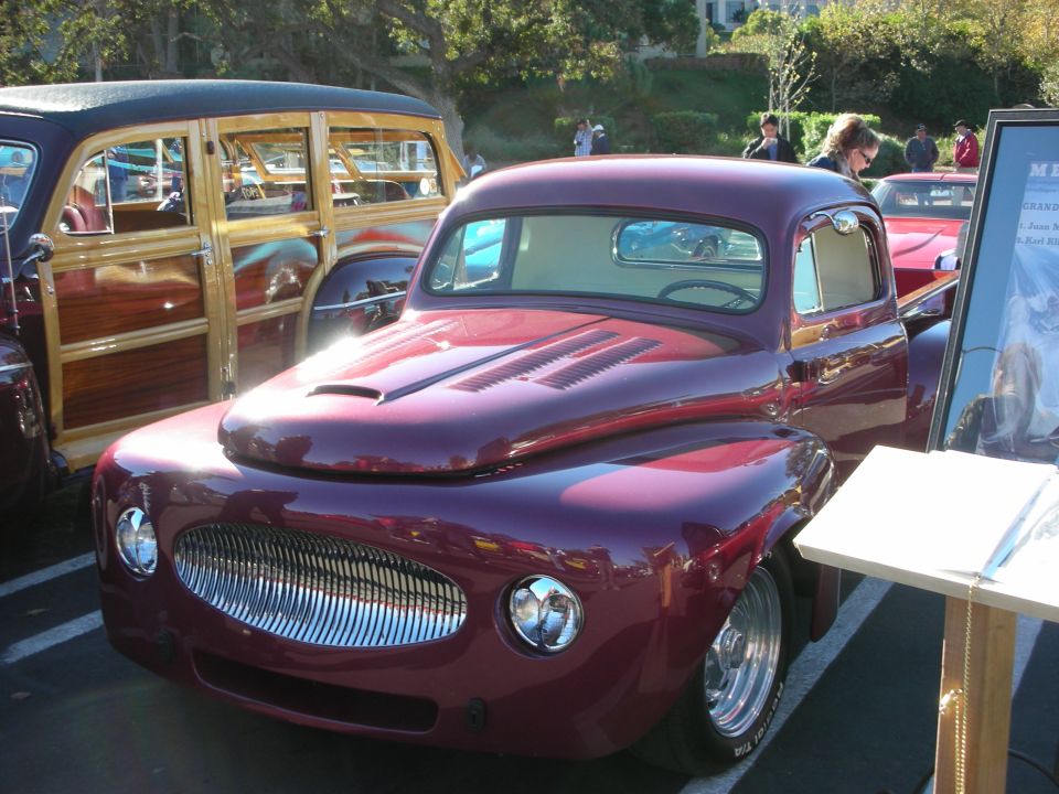 Maroon custom pickup truck with chrome grille and hood vents, parked next to a wood-paneled station wagon