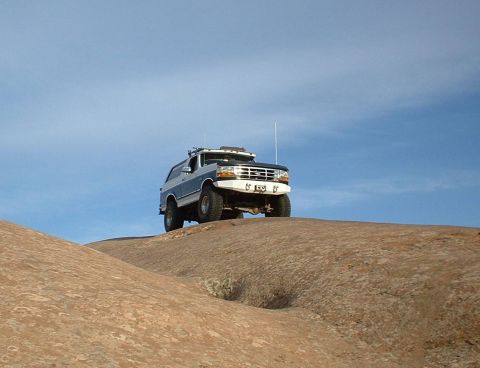 1993 Ford Bronco - A two-tone Ford Bronco navigates a rocky terrain under a clear blue sky.