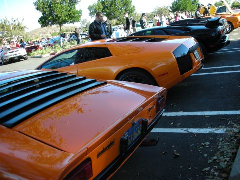 1992 Ford Crown Victoria - Multiple exotic cars, including a pair of orange Lamborghinis and a black supercar, are parked in a lot.