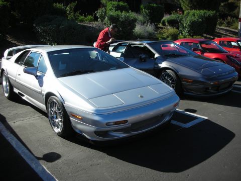 1992 Ford Crown Victoria - A silver sports car is parked in a lot with other vehicles, including a dark gray sports car and red sports cars in the background.