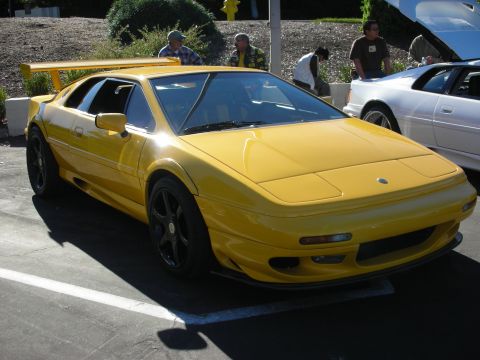 1992 Ford Crown Victoria - A yellow sports car is parked in a lot next to a white car with its hood open.