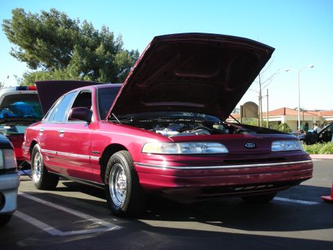 1992 Ford Crown Victoria - A red 1992 Ford Crown Victoria sedan is parked with its hood open, revealing the engine bay.