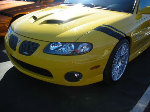 1992 Ford Crown Victoria - A yellow Pontiac GTO is parked next to another vehicle, showing its front grille and headlights.