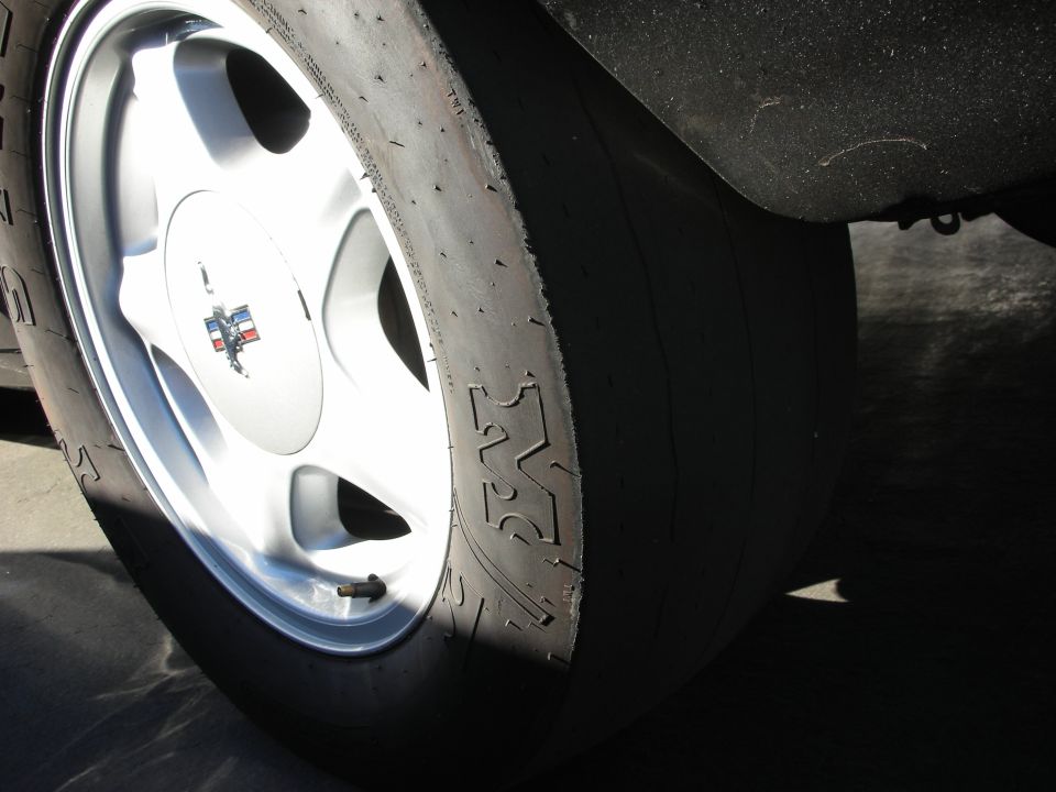 Close-up of a racing tire and silver wheel with a tri-color emblem