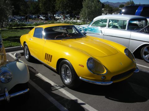 1992 Ford Crown Victoria - A bright yellow Ferrari 275 GTB is parked in a lot, its iconic design alongside other vintage automobiles.