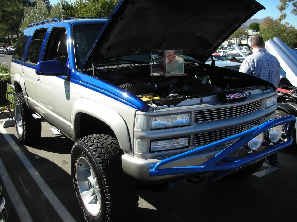 Silver and blue Chevrolet Tahoe with hood open, aftermarket blue brush guard, and large tires