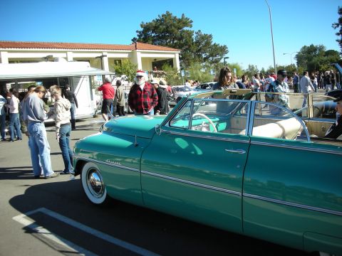 1992 Ford Crown Victoria - A teal convertible is parked at an outdoor event with people milling around.