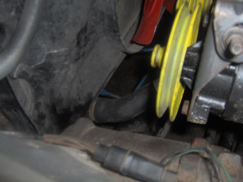 1978 Ford Bronco - Close-up view of engine components, including a yellow pulley and a red fan blade, with visible wiring and hoses.
