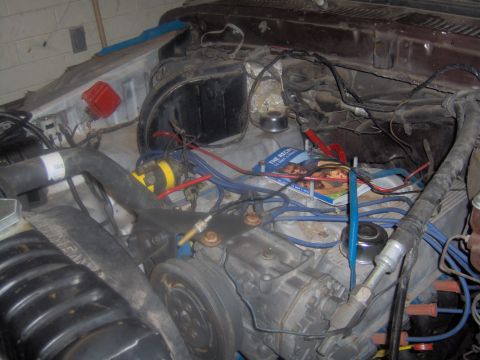1978 Ford Bronco - The engine bay is cluttered with various components and wiring, with a magazine resting on the engine block.
