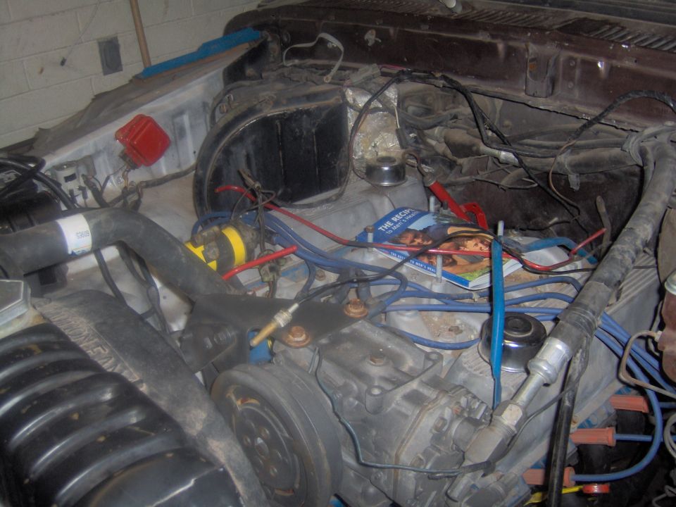 Engine bay with wires, hoses, and a magazine on top of the engine. Supermotors.net logo visible