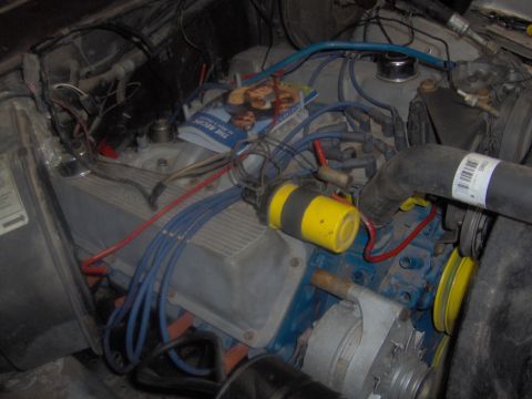 1978 Ford Bronco - A cluttered engine bay with various components and a magazine obscuring part of the engine.