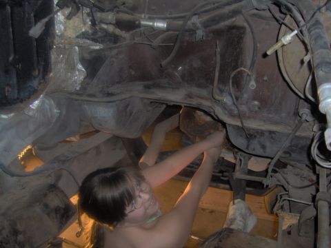 1978 Ford Bronco - A person works on the underside of a vehicle, with visible frame and exhaust components.