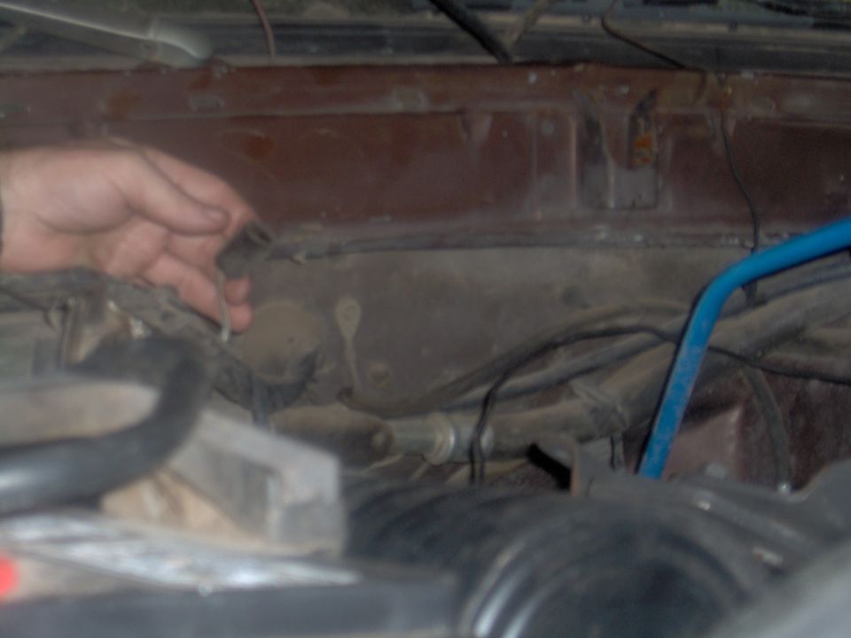 Hand holding an unidentified electrical connector near the firewall in an engine bay