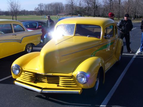 1991 Ford Probe - A bright yellow hot rod with green racing stripes is parked in a lot with other vehicles.