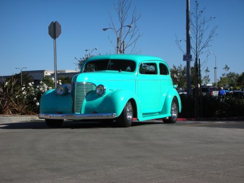 1992 Ford Crown Victoria - A bright turquoise sedan, modified into a hot rod, is parked in a lot under a clear blue sky.